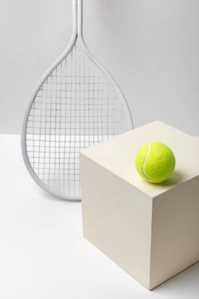 Яскраво-жовтий тенісний м'яч на кубі біля ракетки на білому тлі — стокове фото