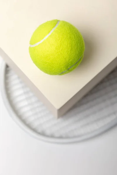 Selective focus of bright yellow tennis ball on cube and racket on white background — Stock Photo