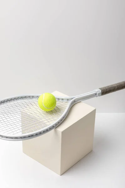 Palla da tennis gialla brillante con racchetta su cubo su sfondo bianco — Foto stock