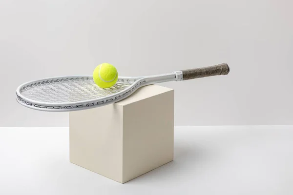 Yellow tennis ball with racket on cube on white background — Stock Photo