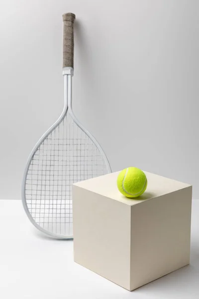 Tennis racket and bright yellow tennis ball on cube on white background — Stock Photo