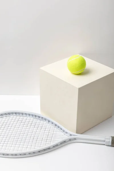 Tennis racket and bright yellow tennis ball on cube on white background — Stock Photo