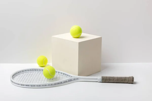 Tennis racket and bright yellow tennis balls on cube on white background — Stock Photo