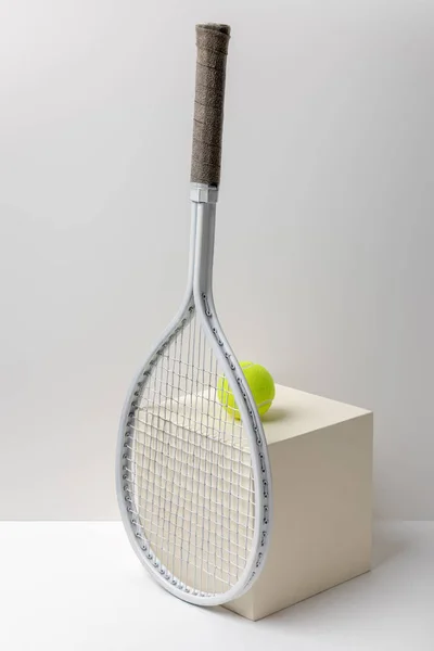 Tennis racket and bright yellow tennis ball on cube on white background — Stock Photo