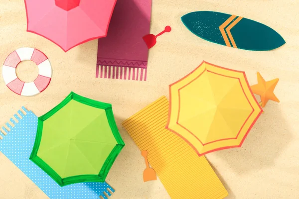 Top view of paper beach with umbrellas, towels and surfboard on textured sand — Stock Photo