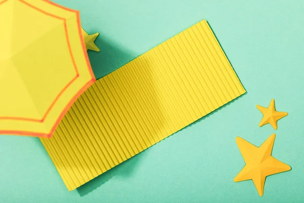 Top view of paper cut yellow towel and umbrella near starfishes on turquoise background — Stock Photo