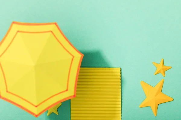 Top view of paper yellow towel and umbrella near starfishes on turquoise background — Stock Photo