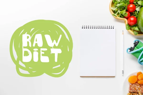 Top view of blank notebook near diet food and skipping rope on white background with with raw diet lettering — Stock Photo