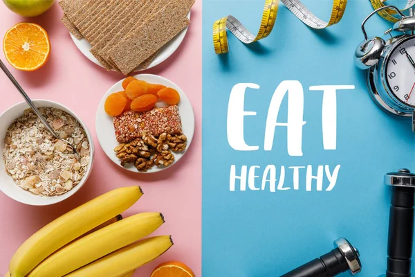 Top view of fresh fruits, crispbread and breakfast cereal on pink and dumbbells and measuring tape on blue background with eat healthy lettering — Stock Photo