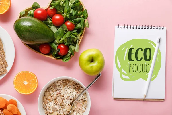 Vista superior de alimentos de dieta fresca y cuaderno con letras de productos ecológicos sobre fondo rosa - foto de stock