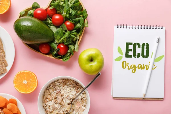 Vista dall'alto di alimenti dietetici freschi e notebook con parole eco biologiche su sfondo rosa — Foto stock