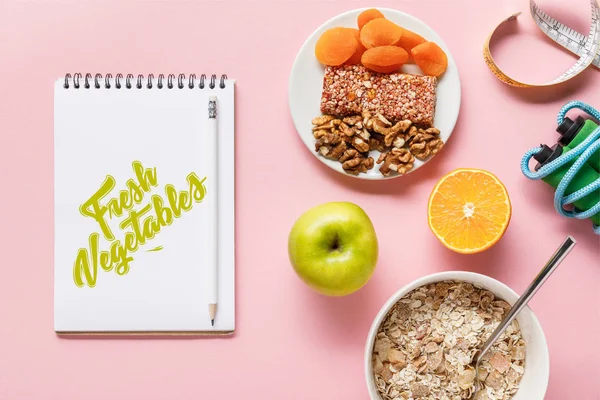 Draufsicht auf frische Ernährung, Maßband, Springseil und Notizbuch mit frischem Gemüse-Schriftzug auf rosa Hintergrund mit Kopierplatz — Stockfoto