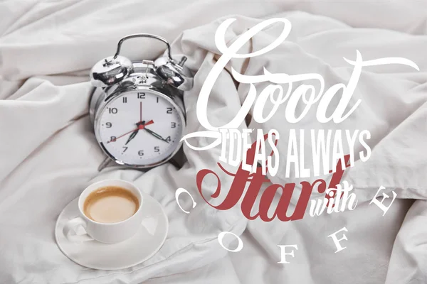 Кофе в белой чашке на блюдце возле серебряного будильника в постели с хорошими идеями всегда начинаются с иллюстрации кофе — стоковое фото