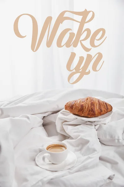 Croissant fresco na placa perto do café na xícara branca no pires na cama com ilustração do despertar — Fotografia de Stock