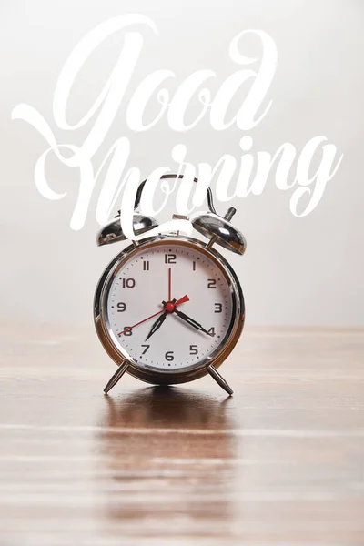 Silver alarm clock on wooden table isolated on grey with good morning illustration — Stock Photo