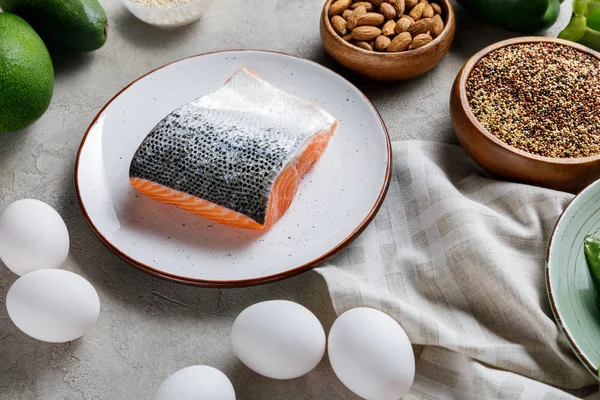 Frischer roher Lachs auf weißem Teller in der Nähe von Nüssen und Eiern, ketogene Speisekarte — Stockfoto
