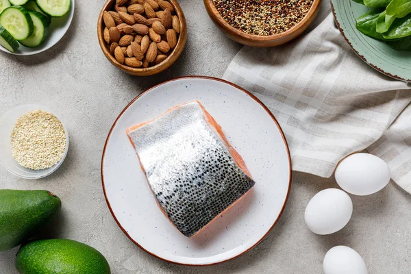 Frischer roher Lachs auf weißem Teller in der Nähe von Nüssen, grünem Gemüse und Eiern, ketogene Speisekarte — Stockfoto