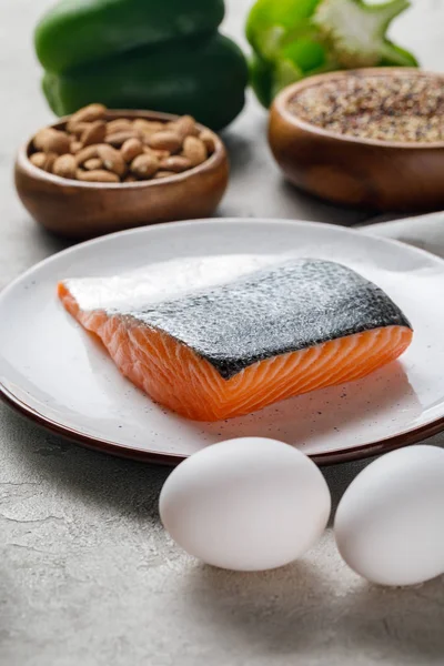 Selective focus of fresh raw salmon on white plate near nuts and eggs, ketogenic diet menu — Stock Photo