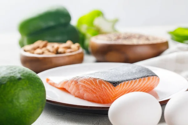 Selective focus of fresh raw salmon on white plate near avocado and eggs, ketogenic diet menu — Stock Photo
