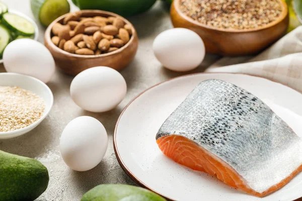 Fresh salmon on white plate near nuts and eggs, ketogenic diet menu — Stock Photo