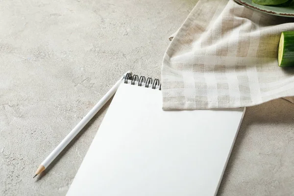 Cuaderno vacío con lápiz en la superficie de textura gris cerca de la servilleta y el pepino, menú de dieta cetogénica - foto de stock