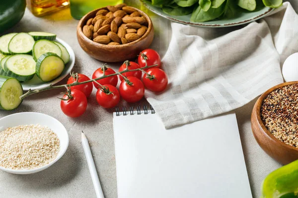 Cuaderno vacío con lápiz en la superficie de textura gris cerca de la servilleta, nueces, tomates y pepino, menú de dieta cetogénica - foto de stock