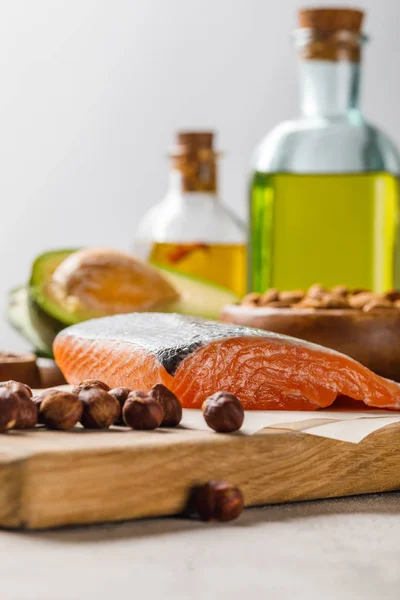 Selective focus of fresh raw salmon, nuts on wooden chopping board near oil isolated on grey, ketogenic diet menu — Stock Photo