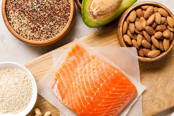Top view of fresh raw salmon on wooden chopping board near nuts, groats and avocado, ketogenic diet menu — Stock Photo