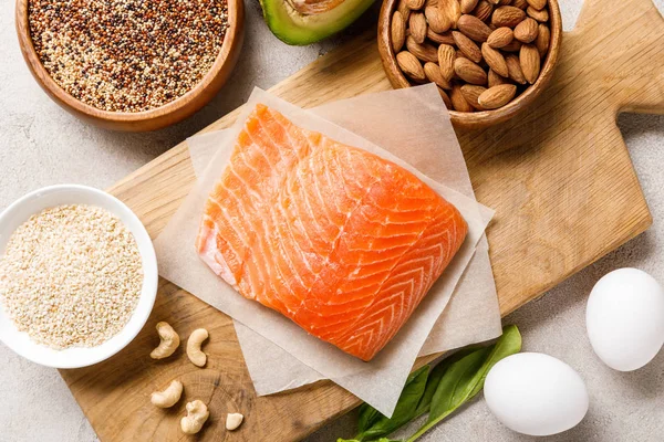 Vista dall'alto del salmone fresco crudo sul tagliere di legno vicino a noci, semole e uova, menu dieta chetogenica — Foto stock