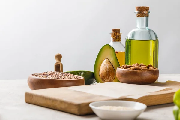 Nuts and avocado on wooden chopping board near oil and groats isolated on grey, ketogenic diet menu — Stock Photo