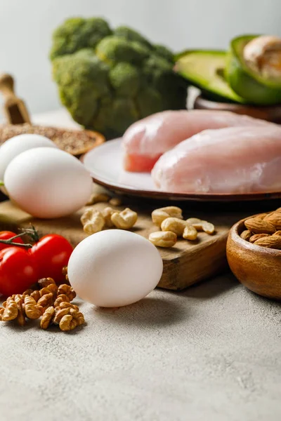 Foco seletivo de peitos de frango crus frescos na placa branca perto de nozes e ovos, menu de dieta cetogênica — Fotografia de Stock