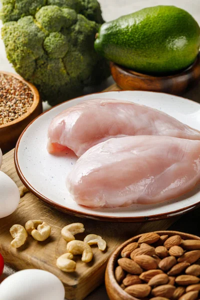 Fresh raw chicken breasts on white plate near nuts, green vegetables and eggs, ketogenic diet menu — Stock Photo