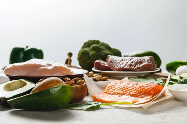 Fresh raw salmon, meat and chicken breasts near green vegetables isolated on grey, ketogenic diet menu — Stock Photo