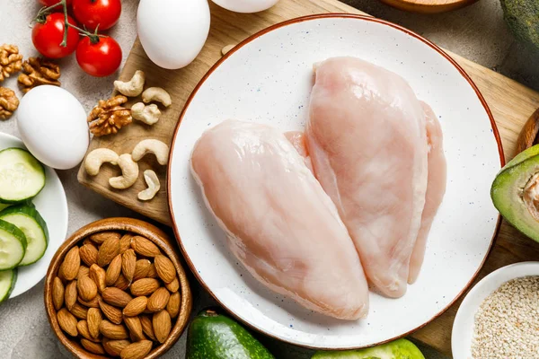 Vue du dessus des poitrines de poulet crues fraîches près des noix, des œufs et des légumes, menu diététique cétogène — Photo de stock