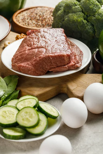 Vista de perto da carne crua na tábua de corte de madeira perto de ovos e pepinos,, menu de dieta cetogênica — Fotografia de Stock