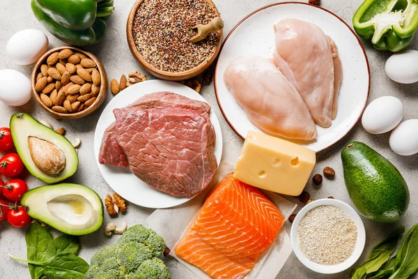 Top view of raw salmon, chicken breasts and meat on white plates near nuts, eggs and vegetables, ketogenic diet menu — Stock Photo