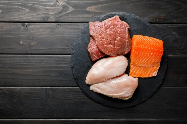 Vue du dessus des poitrines fraîches de saumon cru, de viande et de poulet sur table noire en bois, menu diététique cétogène — Photo de stock