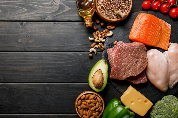 Draufsicht auf frischen rohen Lachs, Fleisch- und Hühnerbrust auf schwarzem Holztisch mit Gemüse und Nüssen, ketogene Speisekarte — Stockfoto