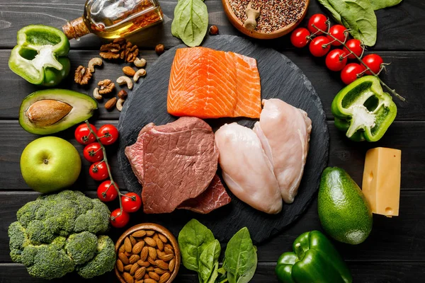 Vue du dessus des poitrines crues de saumon, de viande et de poulet sur table noire en bois avec légumes et noix, menu diététique cétogène — Photo de stock