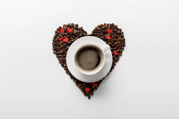 Top view of coffee in cup on saucer with heart made of coffee grains on white background — Stock Photo