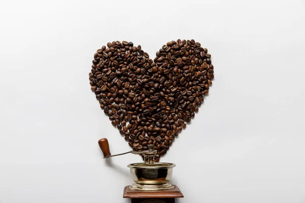 Top view of heart made of coffee grains near vintage coffee grinder on white background — Stock Photo