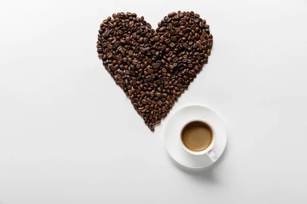 Vista dall'alto del caffè con cuore fatto di chicchi di caffè su sfondo bianco — Foto stock