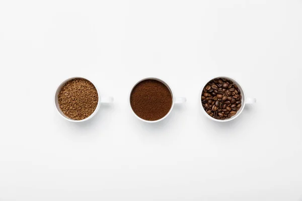 Tendido plano con tres tipos de molienda de café en tazas sobre fondo blanco - foto de stock