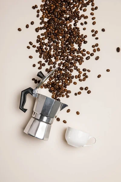 Top view of aluminium coffee pot, cup and scattered fresh coffee beans on beige background — Stock Photo