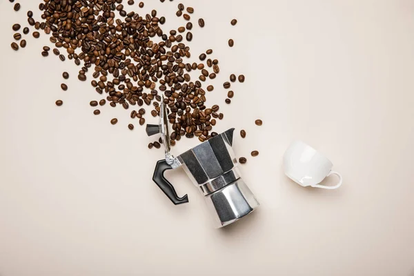 Vista superior de la cafetera de metal, taza y granos de café frescos dispersos sobre fondo beige - foto de stock
