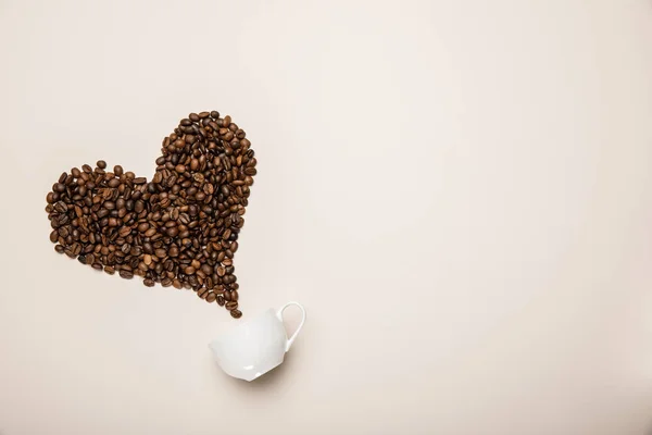 Top view of cup near heart made of coffee grains on beige background — Stock Photo