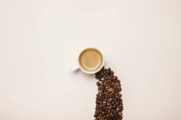 Vista dall'alto della tazza con caffè fresco vicino grani di caffè su sfondo beige — Foto stock