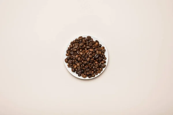 Top view of coffee grains on white saucer on beige background — Stock Photo