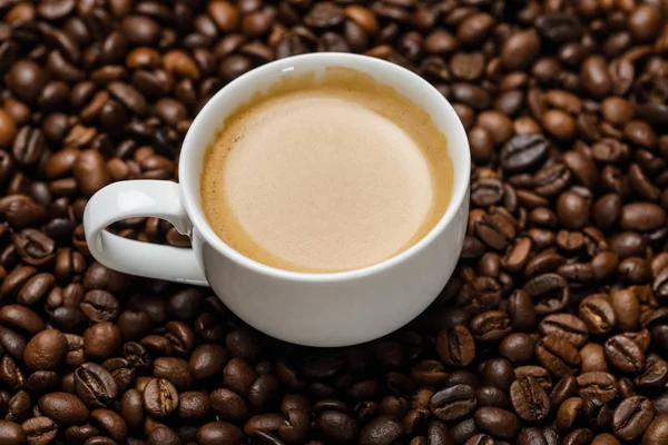 Vista de perto do delicioso café na xícara branca em grãos de café frescos — Fotografia de Stock