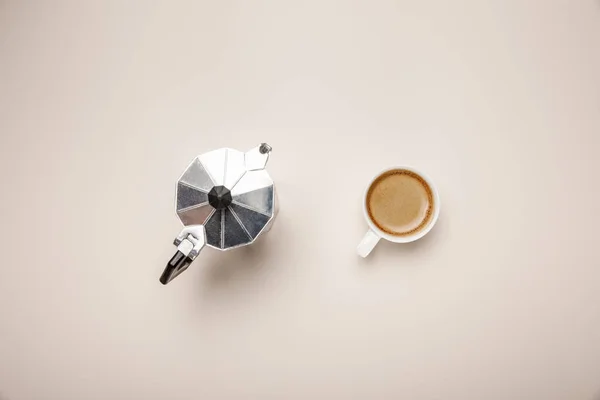 Вид сверху на металлический кофейник и вкусный кофе в чашке на бежевом фоне — стоковое фото